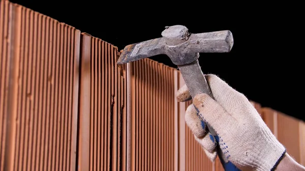 Close up of man hands holding hammer and using it to make an oblong hole on black background. Stock footage. Construction worker demolishing hole at brick wall with a hammer. — 스톡 사진