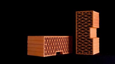 Siyah zemin üzerinde izole hareket eden yuvarlak delikli turuncu tuğlaları kapatın. Stok görüntüleri. Yeni tuğla ev için malzemeler..