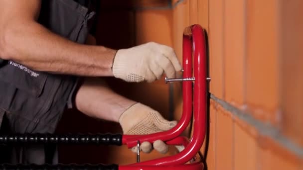 Side view of a worker hanging heavy metal object on the wall made of ceramic blocks. Stock footage. Close up of male hands in protective gloves tightening the screw inside the red ceramic blocks. — 비디오