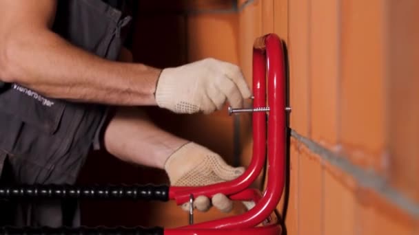 Vue latérale d'un travailleur suspendu à un objet en métal lourd sur le mur en blocs de céramique. Images d'archives. Gros plan des mains masculines dans des gants de protection serrant la vis à l'intérieur des blocs de céramique rouge . — Video