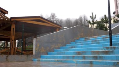 Wooden pavilion in raining season located near concrete stairs on grey heavy sky background. Stock footage. Covered gazebo under the rain in late autumn.