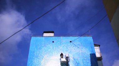 Bir sanatçının mavi bulutlu arka planda nefes kesici graffiti çizmek için vinç kullanmasının alt görüntüsü, zaman aşımı etkisi. - Sanat. Sokak sanatı konsepti, sprey boyalı bir adam.