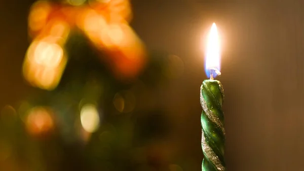 Beautiful green candle burning on a Christmas Eve with the decorated blurred Christmas tree on the background. Concept. Burning New Year candle, time lapse effect.