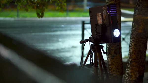 Projetor luzes feixe para mostrar foto e vídeo materiais na rua à noite no fundo da estrada vazia. Arte. Vídeo projetor e tripé ao ar livre na cidade . — Fotografia de Stock