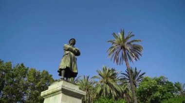 Yeşil ağaçların ve gökyüzünün arka planında duran insan heykeli. Başla. Palmiye ağaçları ve mavi gökyüzünün arka planında güzel bir insan heykeli görünüyor.