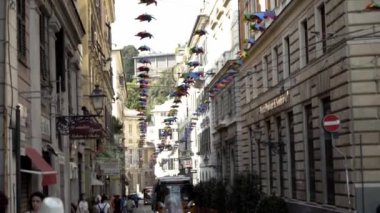 Cenova, İtalya-Haziran 2019: Avrupa mimarisi ve yürüyen insanlarla dolu dar bir sokak. Başla. Yürüyen insanlar ve turistlerle dolu renkli kağıt çelenklerle süslenmiş güzel Avrupa caddesi