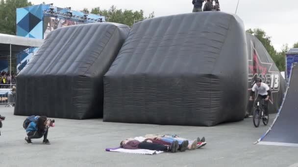 Jekaterinburg, Russia-August, 2019: Cyklisten hoppar över människor. Det är Acion. Farligt stunt av professionell cyklist hoppar över liggande människor på bakgrund av ramper — Stockvideo