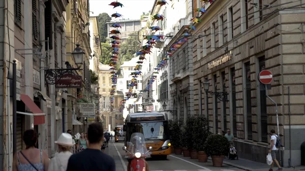 Gênes, Italie-Juin 2019 : Rue étroite avec l'architecture européenne et les gens qui marchent. L'action. Belle rue européenne décorée avec des guirlandes en papier coloré avec des gens qui marchent et des touristes — Photo