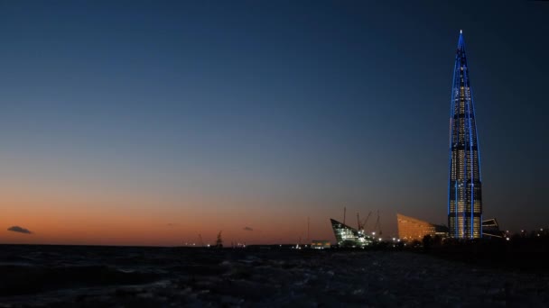 Vista del rascacielos junto al río por la noche. Concepto. Hermoso rascacielos moderno en la orilla de la bahía por la noche — Vídeos de Stock