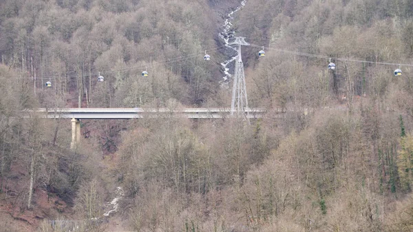 Herfst landschap van de berghelling bedekt door gele bomen en de brug boven smalle beek. Voorraadbeelden. Kabelbanen boven de bomen bevroren. — Stockfoto