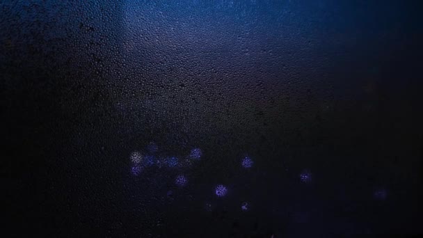 Close-up of window with raindrops on blurred background of lights. Concept. Dim lights shine through dark window blurred by raindrops — Stock Video