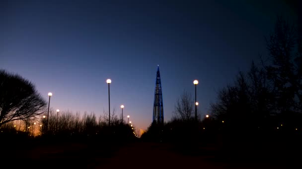 Vista noturna do centro de negócios de Gazprom, centro de Lakhta no fundo colorido do pôr do sol, Rússia, São Petersburgo. Conceito. Belo arranha-céu e a silhueta do parque da cidade . — Vídeo de Stock