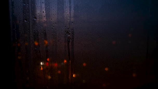 Gros plan de la goutte de pluie sur la fenêtre en verre en saison des pluies avec le fond des lumières de la ville floues. Concept. Incroyables lumières colorées de la rue derrière la fenêtre humide . — Video