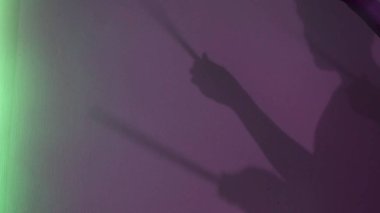 Mor arka planda davul çubuğu olan genç davulcu silueti. Kavram. Neon lambaların, müziğin ve sanat konseptinin altında davul çalıyormuş gibi yapan erkek gölgesi.