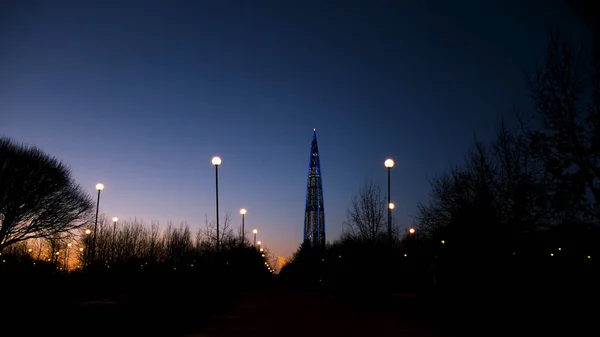 Vista noturna do centro de negócios de Gazprom, centro de Lakhta no fundo colorido do pôr do sol, Rússia, São Petersburgo. Conceito. Belo arranha-céu e a silhueta do parque da cidade . — Fotografia de Stock