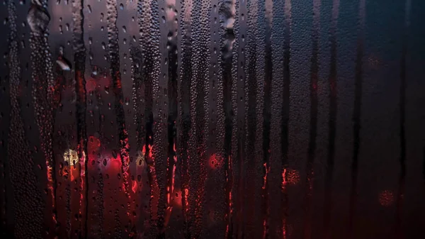 Yağmurlu bir mevsimde cam pencereye düşen yağmur damlalarını kapatır ve arka plandaki bulanık şehir ışıklarını kapatırız. Kavram. Islak pencerenin arkasındaki caddenin inanılmaz renkli ışıkları.. — Stok fotoğraf