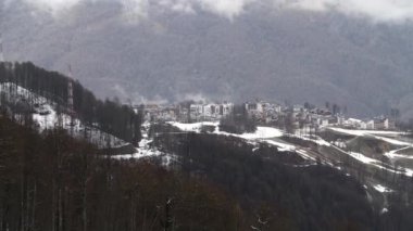 Aerial view of a village located in mountains. Stock footage. Flying over late autumn forest and snowy mountains, ecologycal place for living.