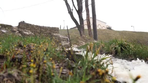 Sluiten van een smalle koude stroom stroomt door het gazon met verdord gras. Voorraadbeelden. Onderaanzicht van het gras en koude beek op grijze lucht achtergrond. — Stockvideo