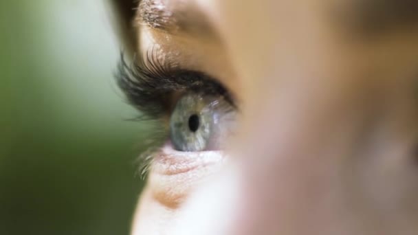 Beautiful female eye of green color with long eyelashes on blurred green background. Action. Close up of female eye under the bright sun outdoors. — Stock video