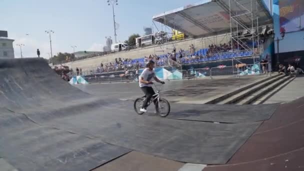 Yekaterinburg, Russia-August, 2019: Cyclist performs stunt on ramp. Action. Young man on bicycle performs dangerous stunts on ramp on background of spectators and city with blue sky — Stock video