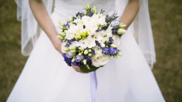 Close up of vivid wedding bouquet at young bride on green grass background, family and celebration concept. Action. Slim woman in white dress holding beautiful wedding bouquet of purple and white — Stock Photo, Image