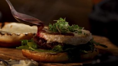 Male chef preparing burger at the restaurant kitchen. Stock footage. Close up of male hands adding wine and cranberry sauce to the tasty delicious beef burger, foodporn.