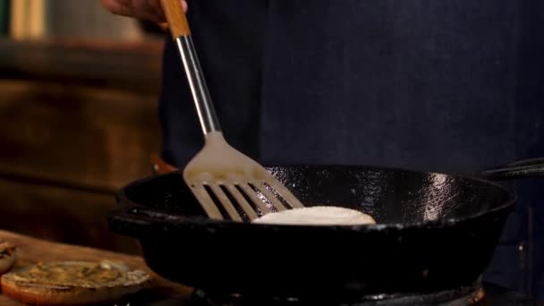 Close up of male cook frying camembert cheese in a black iron pan from the both sides with a metal shovel. Stock footage. Process of food preparation at the restaurant. — Stockvideo