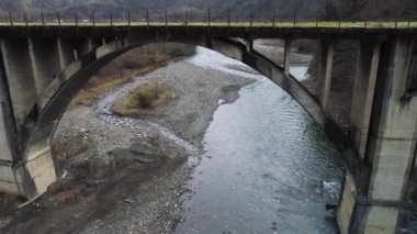 Flying towards the ancient concrete bridge covered by green moss. Shot. Aerial of rural landscape with a small village located in hilly region.