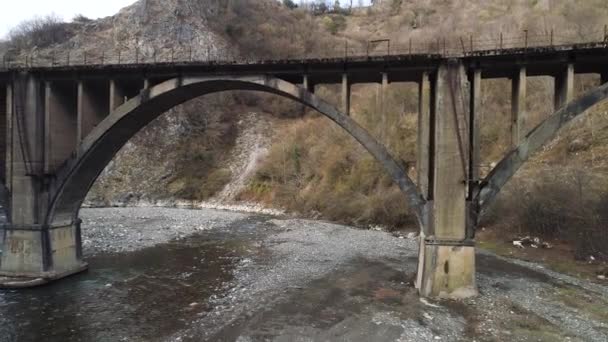 Воздух старого заброшенного моста через почти высохшую реку, экологические проблемы и концепция изменения климата. Выстрел. Летающий над бетонным мостом и узким ручьем в горах — стоковое видео