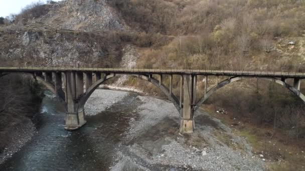 Aerial of an old abandoned mossy bridge over the almost dried out river, ecology problems and climate changing concept. Shot. Flying over the concrete ctone bridge and narrow stream in mountainous — Stock Video