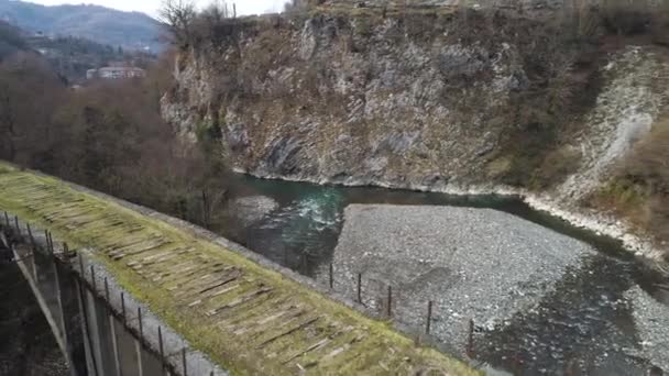 在陡峭的悬崖峭壁附近的冰冷溪流之上的古老的废弃石桥的空中山景。开枪了过了桥就无路可走了. — 图库视频影像