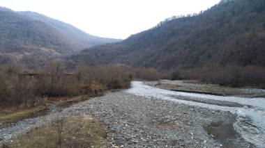 Mountain narrow river and stony shore along high forested mountains. Shot. Aerial autumn landscape, orange hill slopes and the fast flowing cold stream.