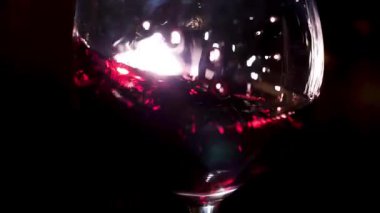 Moving red wine glass over a black background, party and holidays concept. Stock footage. Close up of splashing alcoholic beverage inside the glass.