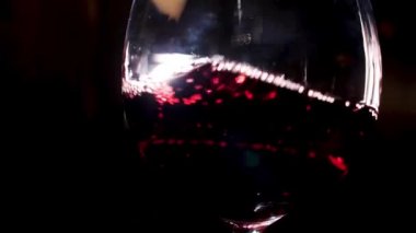 Moving red wine glass over a black background, party and holidays concept. Stock footage. Close up of splashing alcoholic beverage inside the glass.