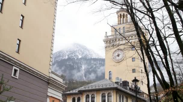 탑의 벽에 시계가 있는 교회 예배당 뒤에 눈덮인 산봉우리가 있다. 주가 영상이요. 옛 유럽 마을의 건축 양식. — 비디오