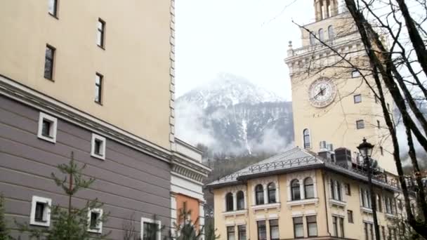 歴史的建造物や雪の山のピークを背景に街の通りに沿って移動車。ストック映像だ。小さな町、道路、美しい建物のヨーロッパの風景. — ストック動画