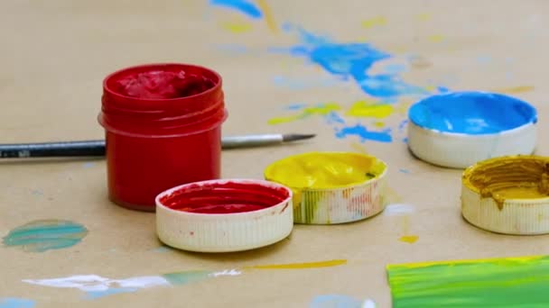 Open small paint jar of red color standing on a table with paint stains and a brush, art and children creativity concept. Stock footage. Close up of bright gouache jar. — Stock Video