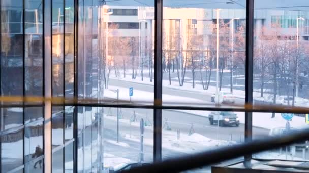 Vista desde el interior de la zona del edificio de negocios a través de la ventana de cristal en una calle de la ciudad con coches en movimiento. Imágenes de archivo. Camino de invierno con coches de conducción y ventana panorámica del centro de negocios . — Vídeos de Stock