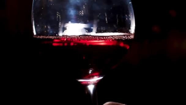 Κουνάει κόκκινο ποτήρι κρασιού με το χέρι του ανθρώπου. Στικ. Κοντινό πλάνο ενός σομελιέ είναι ανακίνηση ποτήρι κρασιού με κόκκινο κρασί στο χέρι του σε ένα σκοτεινό φόντο — Αρχείο Βίντεο