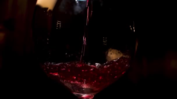 Vin rouge versé dans un verre à vin sur fond noir. Images d'archives. Gros plan de verser de la boisson alcoolisée dans le verre . — Video