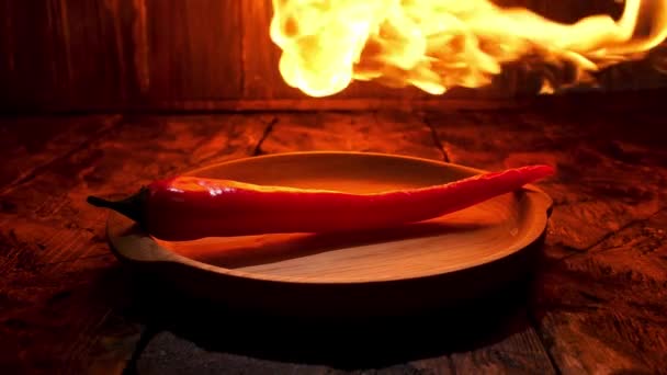 Röd varm chili peppar på svart bakgrund med lågor, kryddig mat koncept. Lagerbilder. Närbild av en peppar som ligger på en träskiva under den varma lågan. — Stockvideo