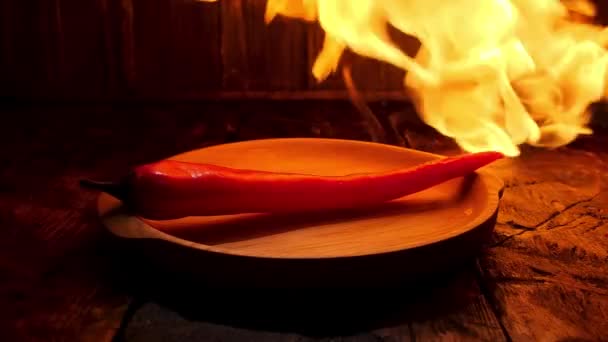 Red hot chilli pepř na černém pozadí s plamenem, pikantní jídlo koncepce. Záběry ze skladu. Detailní záběr pepře ležícího na dřevěné desce pod horkým plamenem. — Stock video