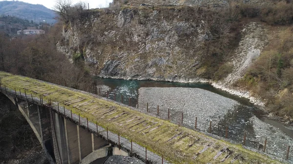 Vista lateral de uma antiga ponte abandonada em um fundo de montanhas na pequena aldeia no final da temporada de outono. Atingido. Ar de ponte de pedra musgosa e o riacho estreito . — Fotografia de Stock