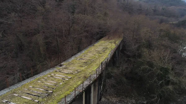 Side view of an old abandoned bridge on a background of mountains in the small village in late autumn season. Shot. Aerial of mossy stone bridge and the narrow brook. — 图库照片