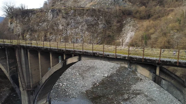 Ar da paisagem montanhosa de ponte de pedra abandonada velha sobre a corrente fria perto de falésias íngremes. Atingido. Voando sobre a ponte que leva a lugar nenhum . — Fotografia de Stock