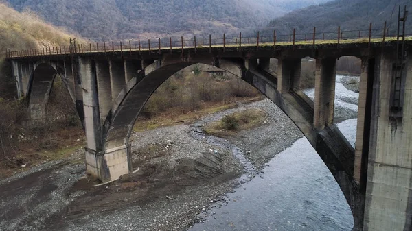 Aeronáutica de uma antiga ponte nebulosa abandonada sobre o rio quase seco, problemas ecológicos e conceito de mudança climática. Atingido. Voando sobre a ponte ctone de concreto e fluxo estreito em montanhoso — Fotografia de Stock