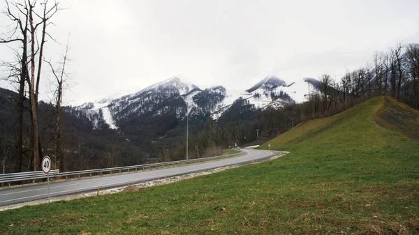 Voiture solitaire sur une route de montagne tourner sur des sommets enneigés et nuageux fond de ciel lourd. Images d'archives. Montagne route voiture voyage vue . — Photo
