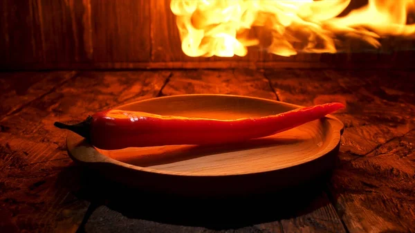 Rote scharfe Chilischote auf schwarzem Hintergrund mit flammendem, würzigem Essenskonzept. Archivmaterial. Großaufnahme einer Paprika, die auf einem Holzbrett unter der heißen Flamme liegt. — Stockfoto