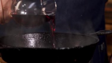 Pouring red wine into frying pan. Stock footage. Close up of chef male hands adding red wine into black iron pan for cooking special sauce.