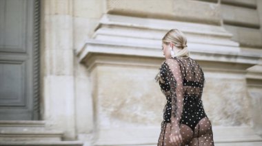 Genç ve cüsseli seksi manken, beyaz noktalı transparan siyah elbiseyi giyip antik katedralin önünde poz veriyor. Başla. Vücut pozitif konsept.